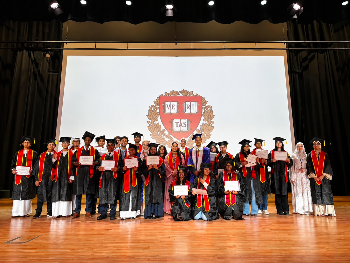 A graduating class of Learn with Leaders students on stage with their certificates in front of the Harvard crest