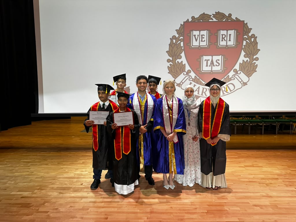 Learn with Leaders students in graduation gowns holding their certificates on stage in front of the Harvard crest